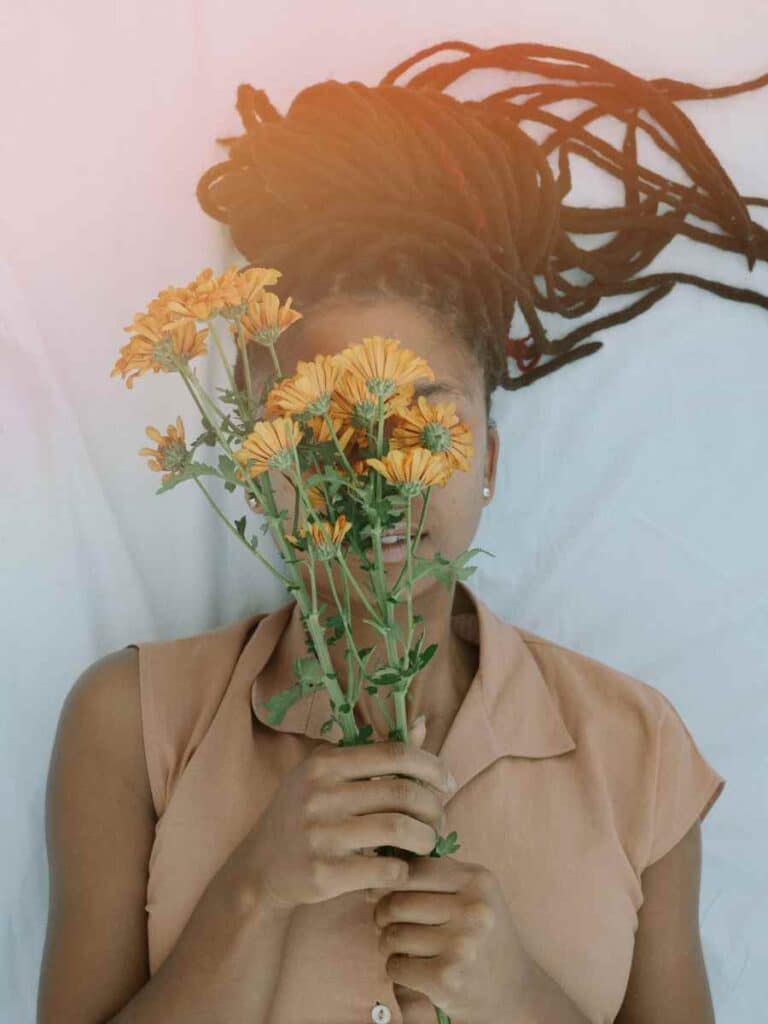 A woman laying down with braids in her hair and holding flowers.