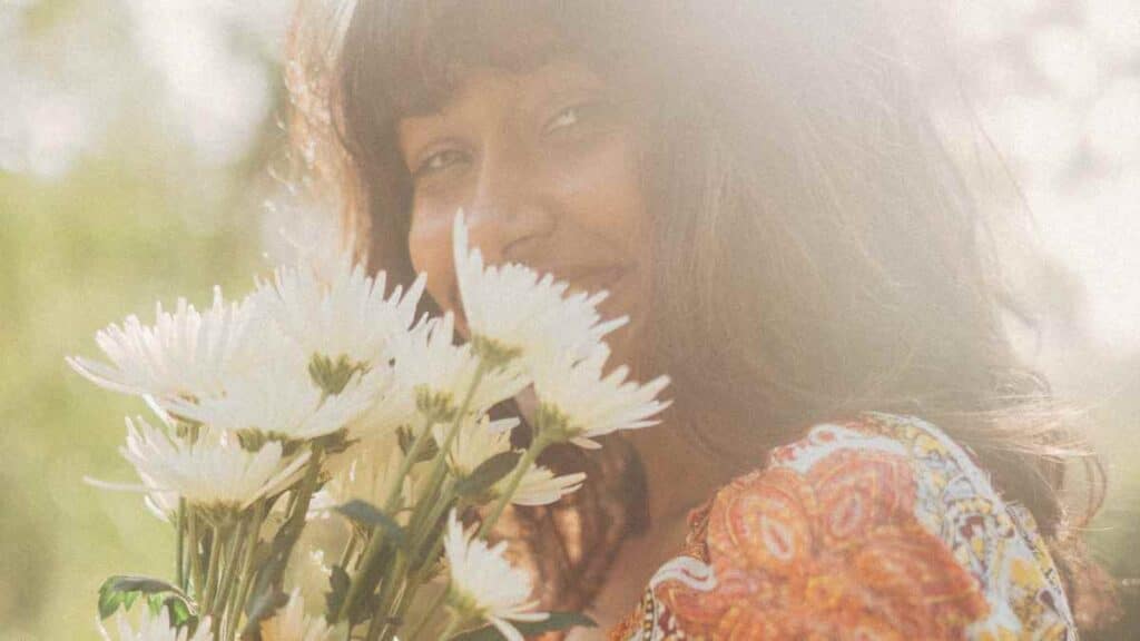 A woman with brown skin holding flowers in nature.